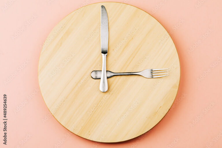 The concept of intermittent fasting and skipping meals. Wooden round tray with cutlery in the form of clock hands